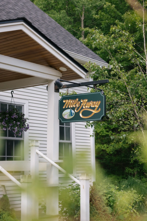 Hanging Mile Away sign on the front porch of the farmhouse surrounded by greenery